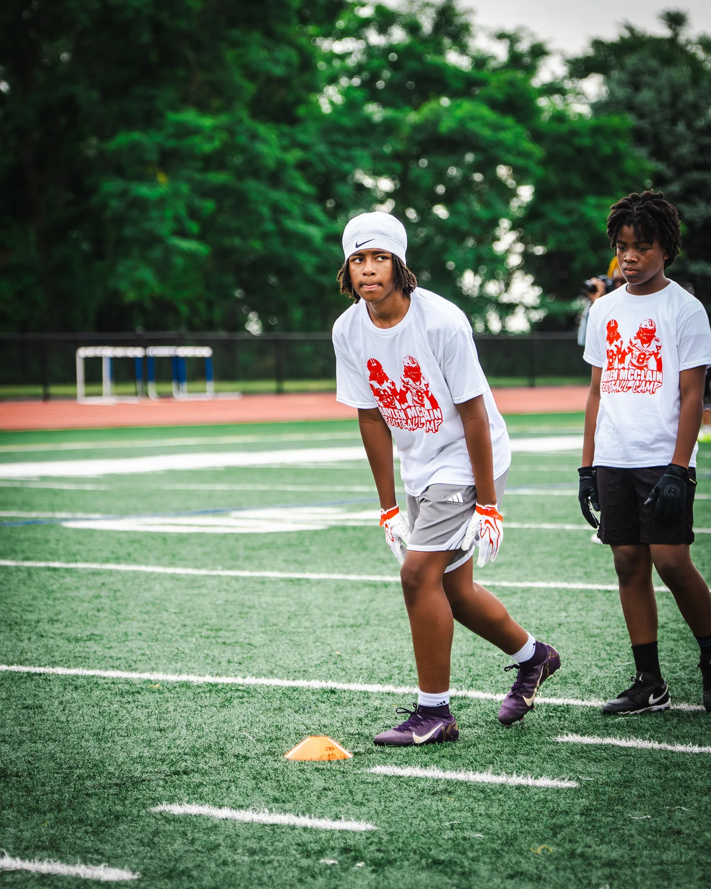 A camper in a Jaylen McClain Youth Football Camp shirt runs a drill on the field.